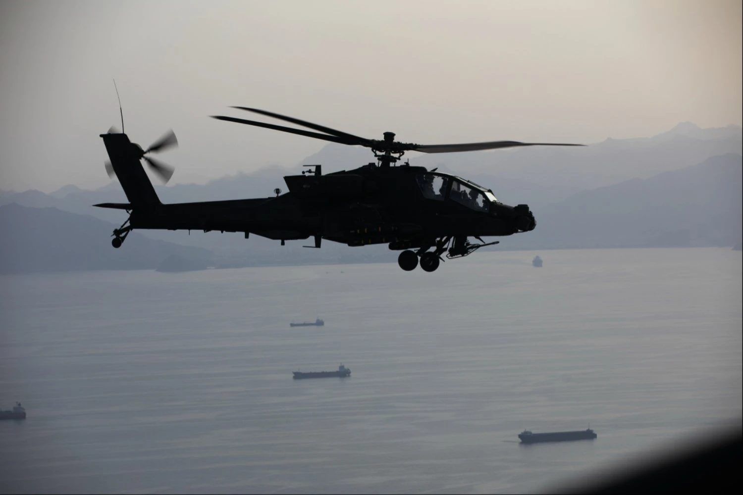 US Army AH-64 Apache helicopters fly over merchant ships in the Strait of Hormuz